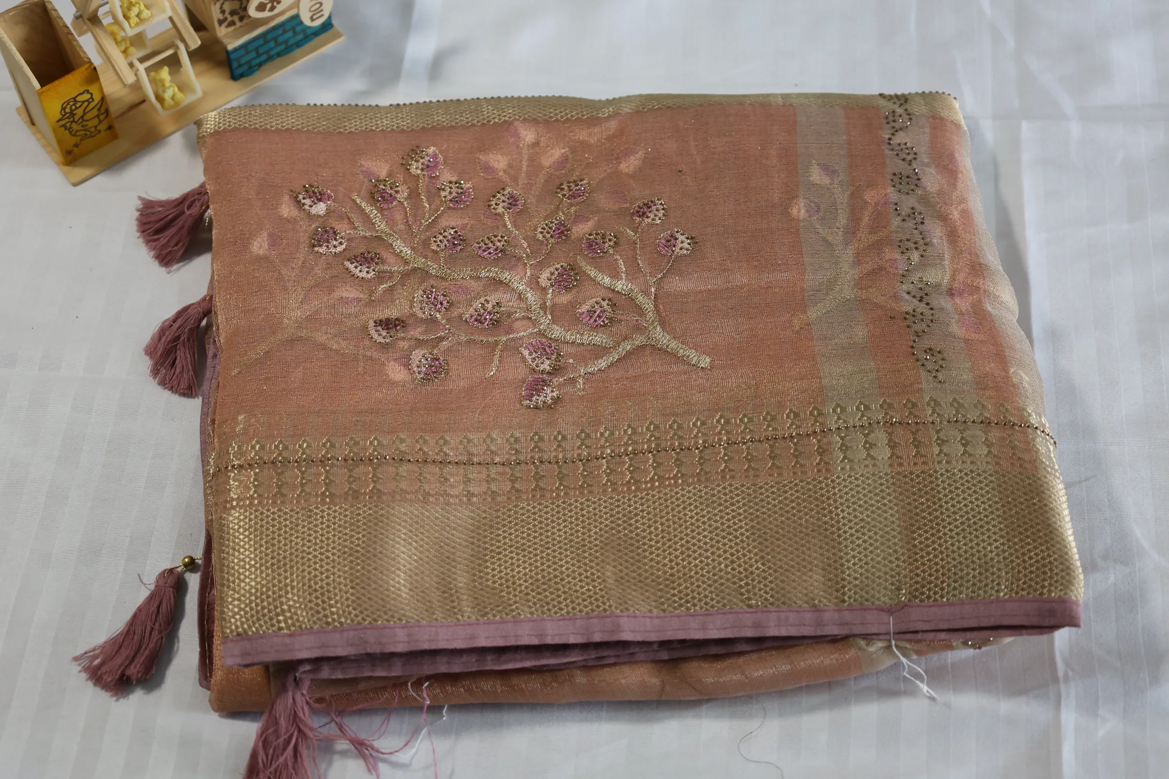 peach-colored silk saree with a golden border and embroidered flowers.